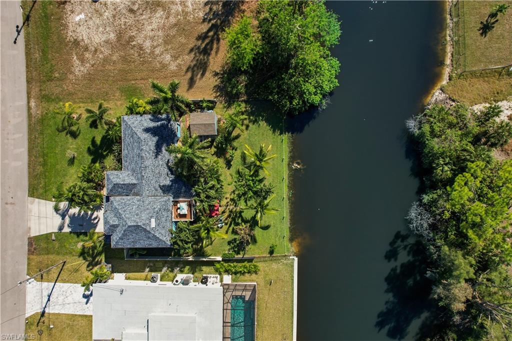 Waterfront property featuring a shingled roof, mature palm trees, a concrete driveway, and a detached shed