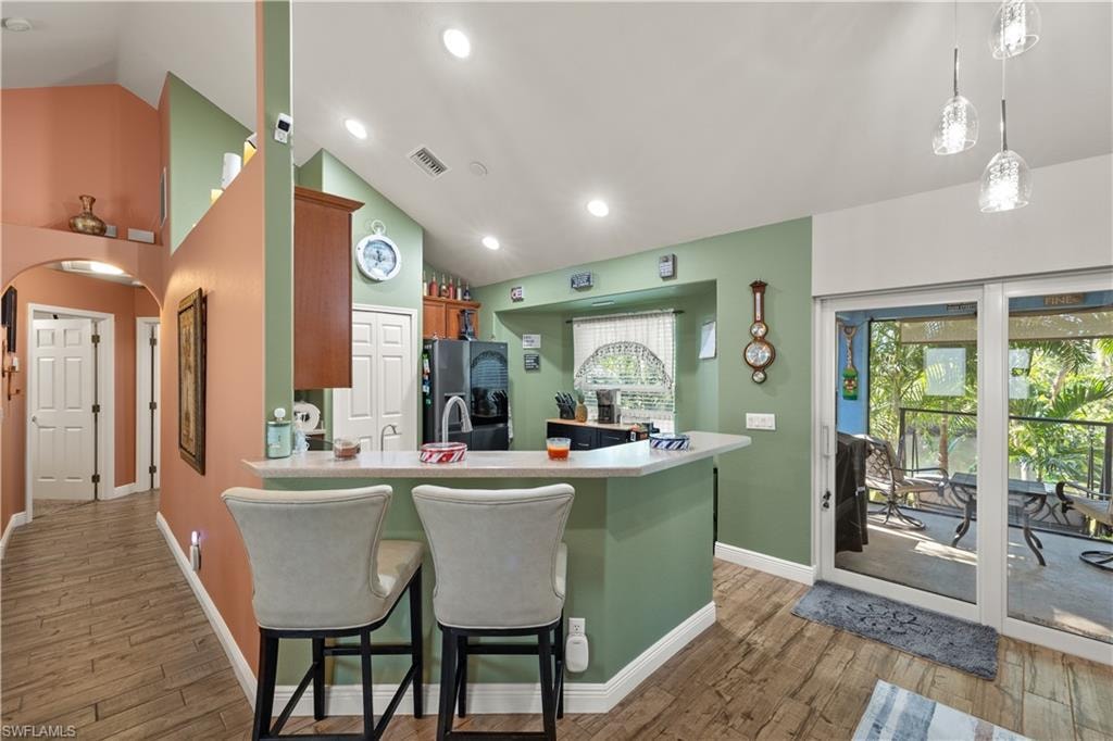 Kitchen with a counter-height breakfast bar featuring a solid surface countertop, wood-finish flooring, and vaulted ceilings