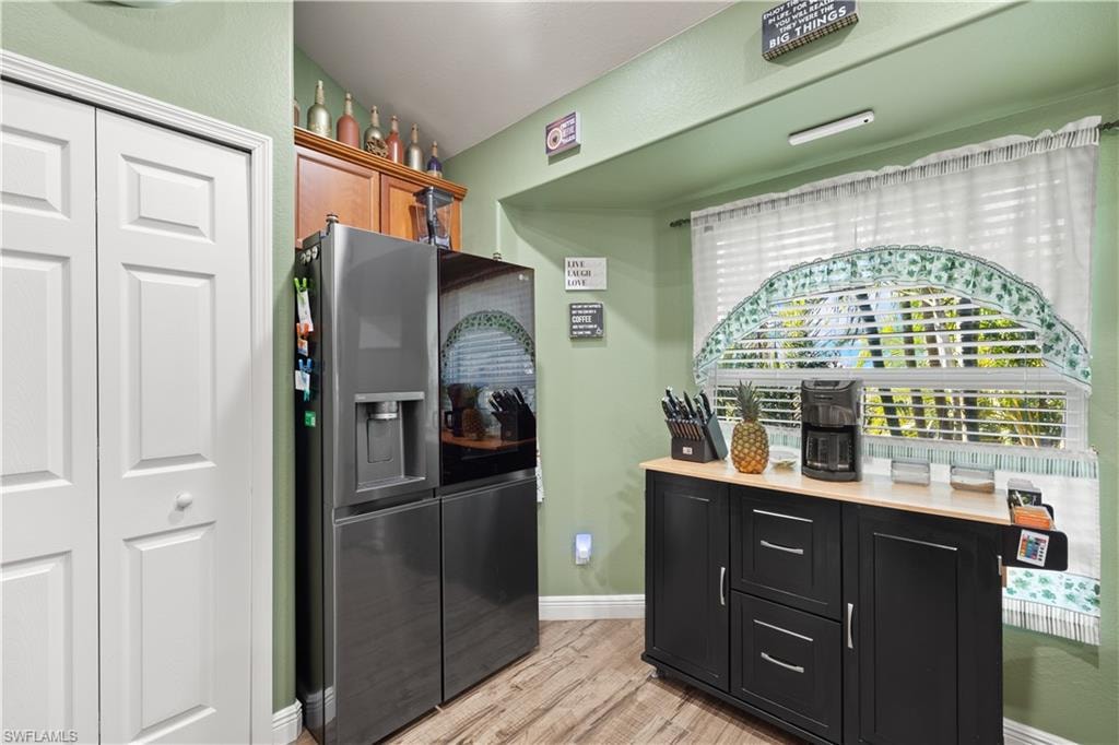 Kitchen area featuring wood-finish flooring, light green walls, a built-in wood cabinet, and a black storage cabinet with a light-toned countertop