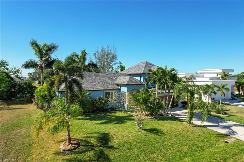 Coastal-style residence featuring a distinctive shingle roof, light blue exterior, and lush tropical landscaping