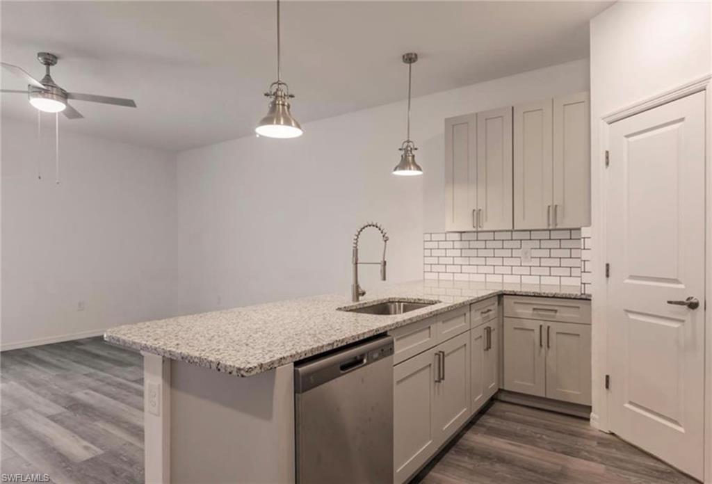 Kitchen featuring light-toned cabinetry, stainless steel dishwasher, white subway tile backsplash, and speckled granite countertops