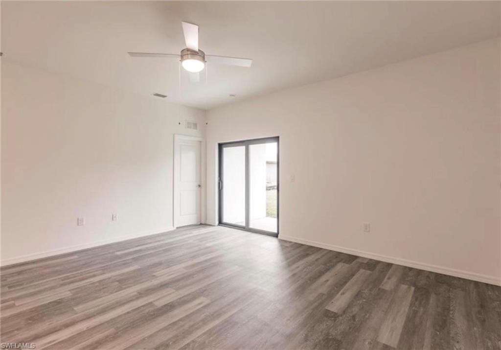 Spacious room featuring wood-finish flooring, a modern ceiling fan, and a white interior door