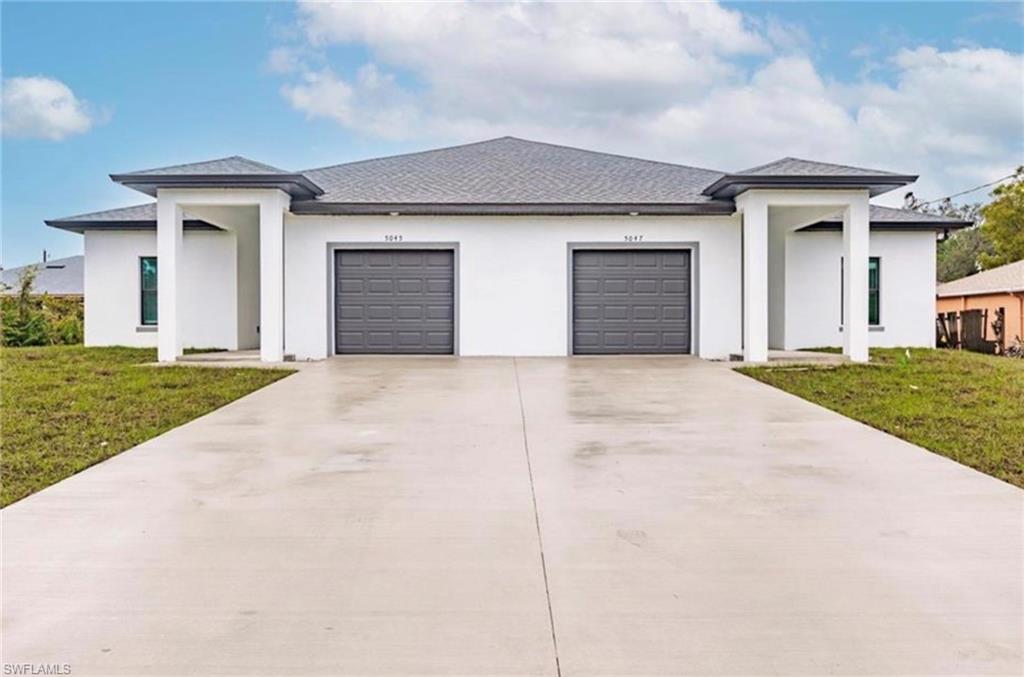 Modern duplex exterior featuring a white stucco finish, dark gray garage doors, and a matching dark gray shingle roof