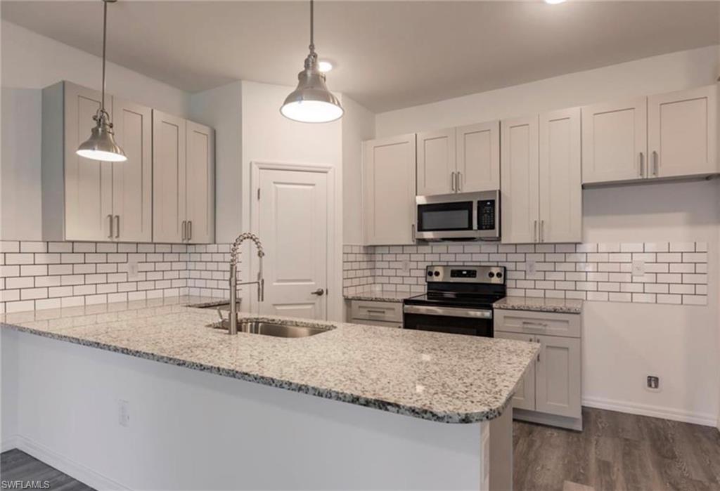 Kitchen featuring granite countertops, subway tile backsplash, stainless steel appliances, pendant lighting, and wood-finish flooring