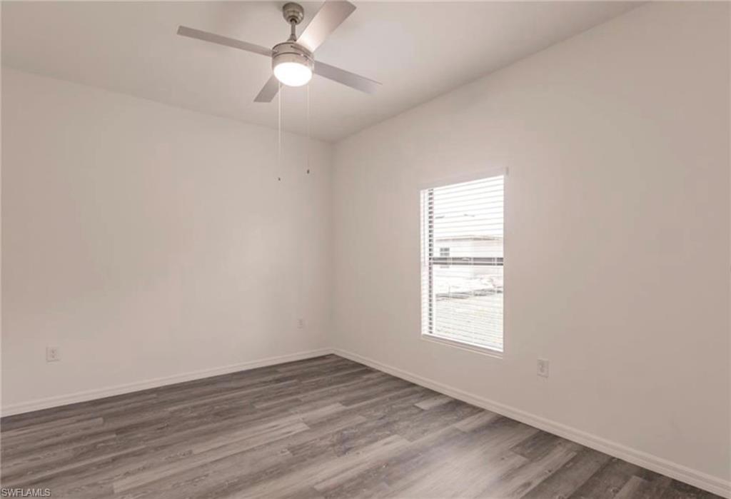 Spacious room featuring gray wood-finish flooring, white walls, and a window with blinds