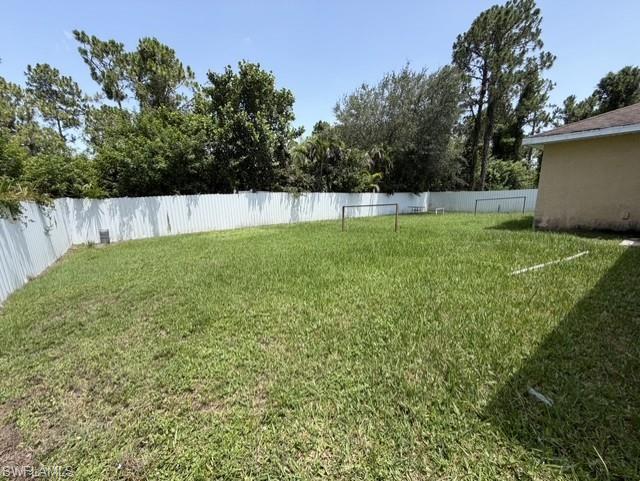 Expansive rear yard featuring green lawn, full perimeter fencing, and mature trees beyond the fence line