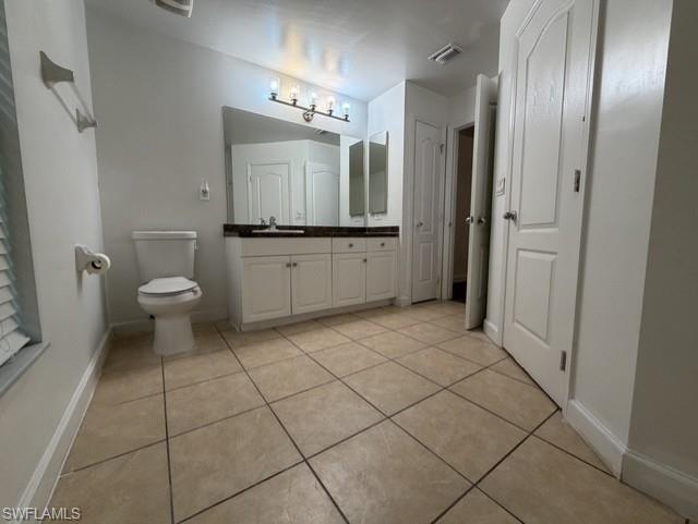Spacious bathroom featuring large format floor tiles, a white vanity with double cabinet storage, a dark countertop, and an illuminated mirror