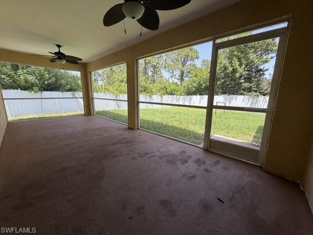 Screened patio featuring a textured floor, two ceiling fans, and a white privacy fence enclosing a grassed area