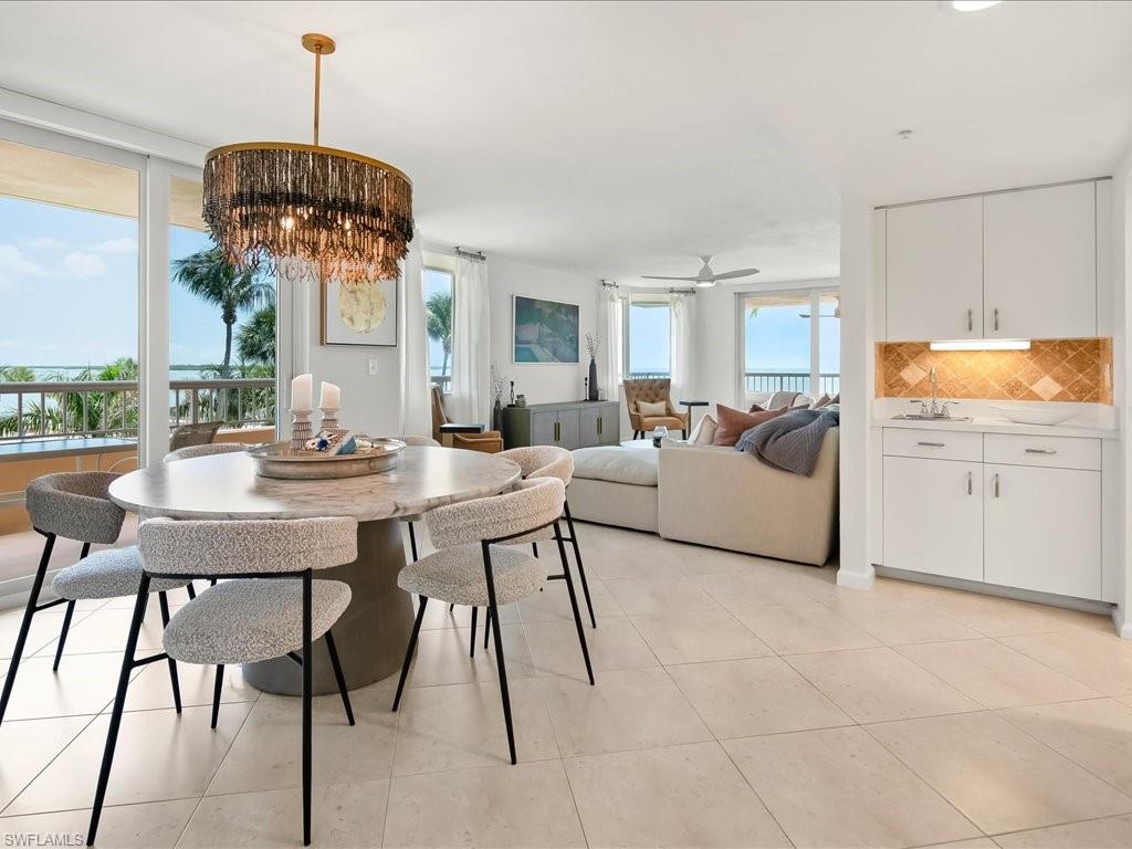 Open-concept living space featuring a dining area with a contemporary chandelier, a built-in wet bar with a tiled backsplash, and light-toned tile flooring throughout