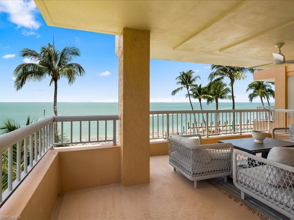 Waterfront balcony with a ceiling fan, offering broad ocean scenery and palm trees
