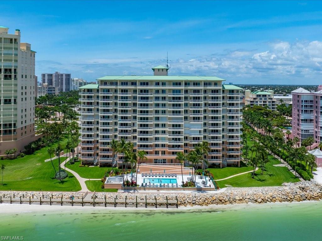 Multi-story condominium building featuring expansive balconies, a waterside swimming pool with lounge seating, and lush surrounding landscaping