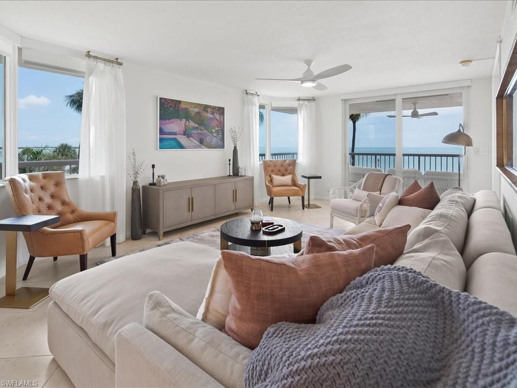 Open-concept living space featuring expansive windows and sliding glass doors, white ceiling fans, light-toned flooring, and a built-in console table