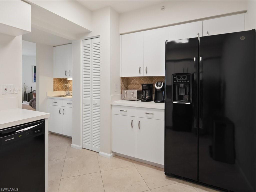 Kitchen featuring a black side-by-side refrigerator, white cabinetry, light countertops, and a patterned tile backsplash