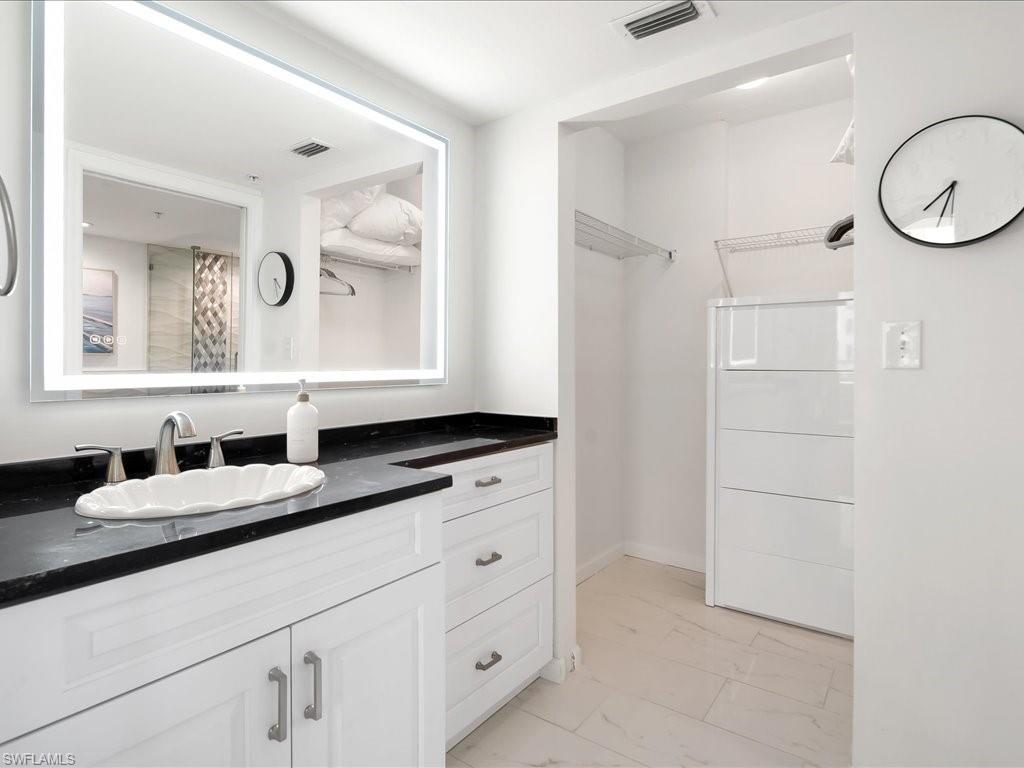 Bathroom vanity with a vessel sink, black countertop, and illuminated mirror