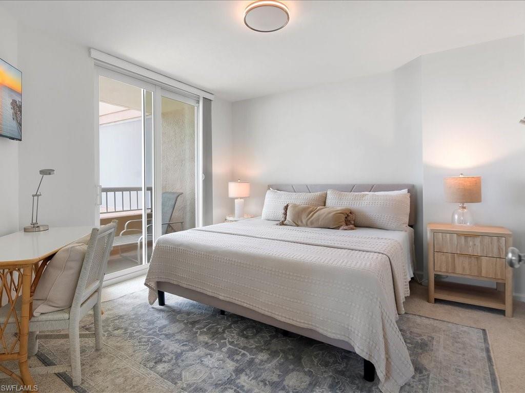 Bedroom featuring a private balcony with sliding glass doors, light gray upholstered bed frame, and wood-finish nightstand