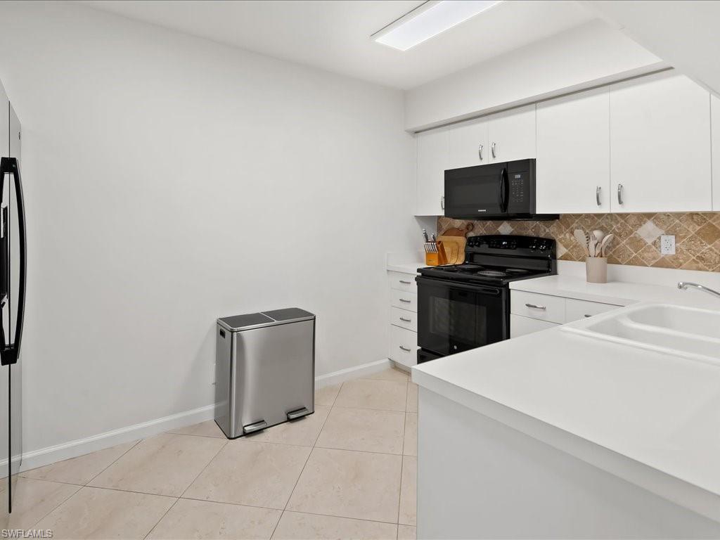 Contemporary kitchen featuring white cabinetry, a black appliance suite, light countertops, and a patterned tile backsplash