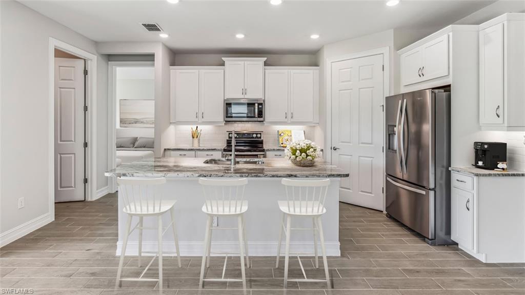Kitchen featuring an island with stone countertop, white shaker-style cabinetry, recessed lighting, and stainless steel appliances