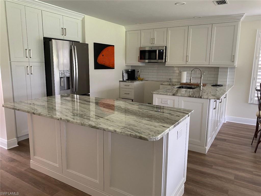 Kitchen with light stone counters, stainless steel appliances, dark wood-style flooring, white cabinetry, and recessed lighting
