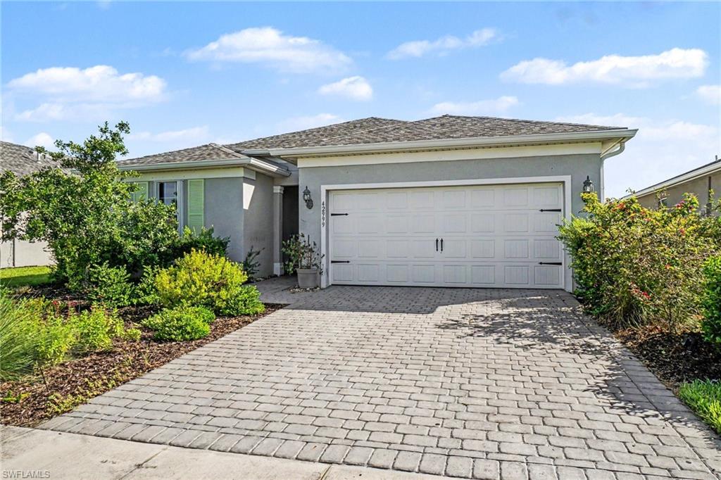 Single-story home featuring a paver driveway, an attached garage, and a stucco exterior