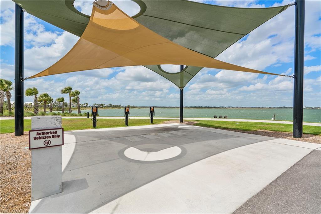 Covered concrete pad with multiple vehicle charging stations, featuring shade sails, waterside access, and surrounding green space with palm trees