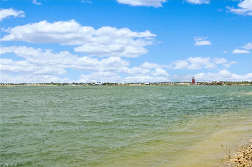 Expansive body of water with a clear shoreline, featuring distant structures under a blue sky with scattered clouds