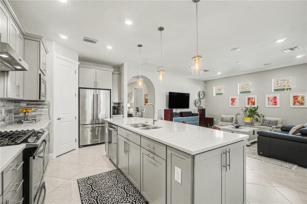 Open-concept kitchen featuring a large island with sink, stainless steel appliances, light gray cabinetry, tiled flooring, and recessed lighting