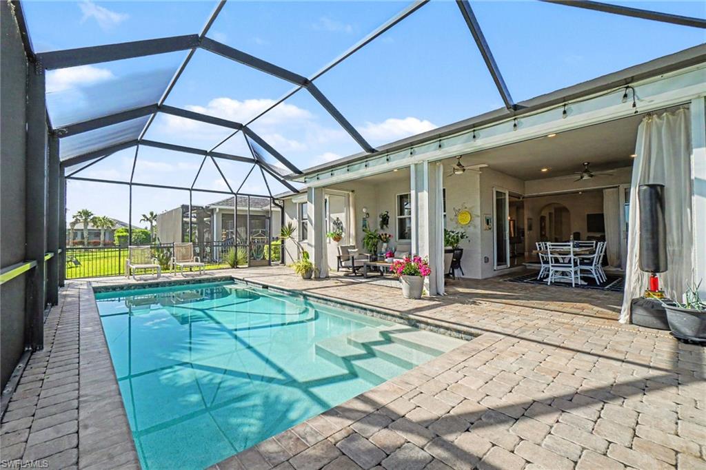 Screened lanai featuring a rectangular pool with integrated steps, paver decking, an outdoor dining area, and a covered patio space with recessed lighting