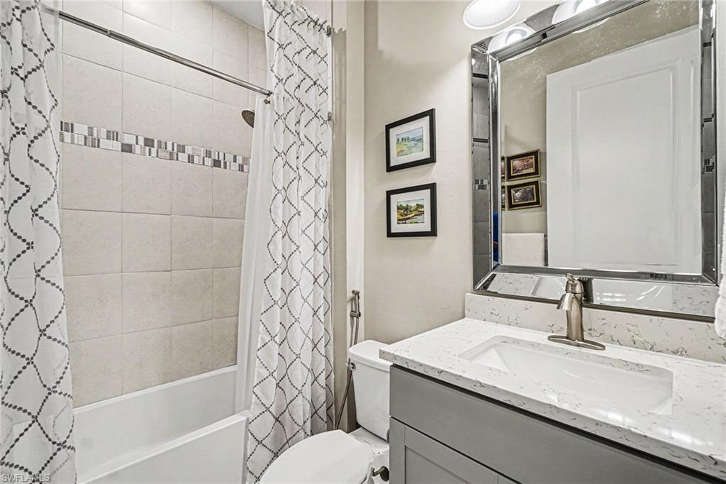 Bathroom featuring a vanity with an integrated sink, a large framed mirror, and a full-size bathtub with tile surround and decorative accent band