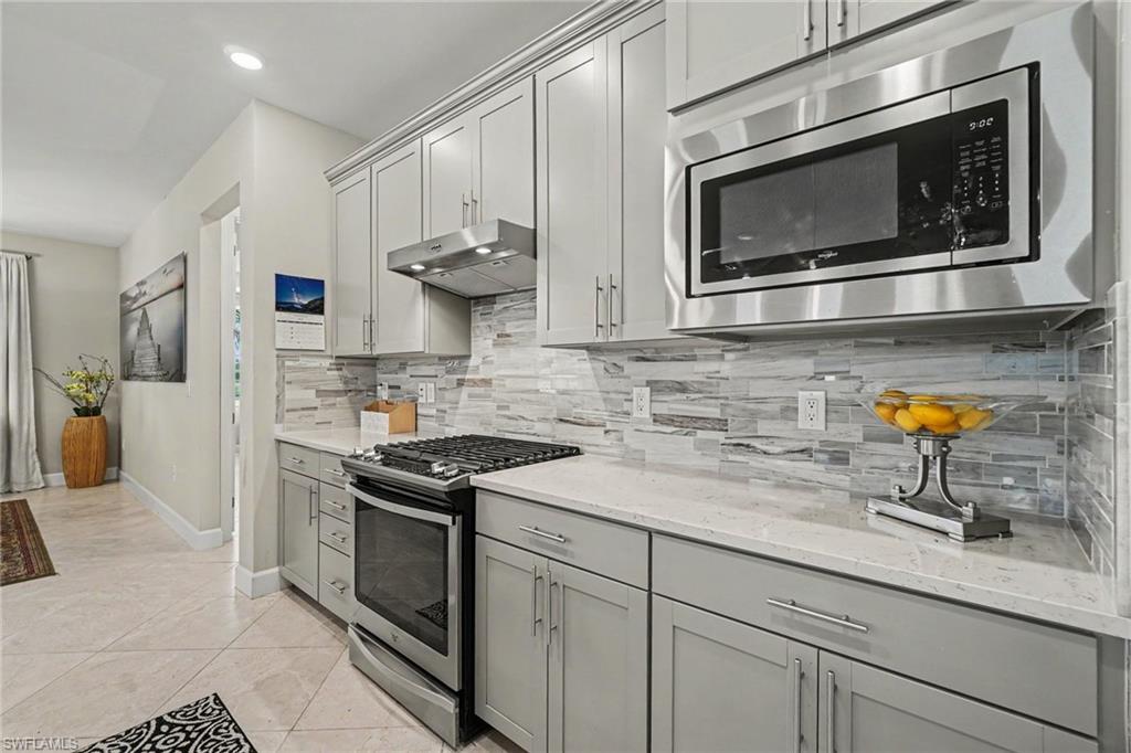 Contemporary kitchen featuring light gray cabinetry with brushed nickel hardware, a stainless steel over-the-range microwave, and a gas range with a matching stainless steel hood