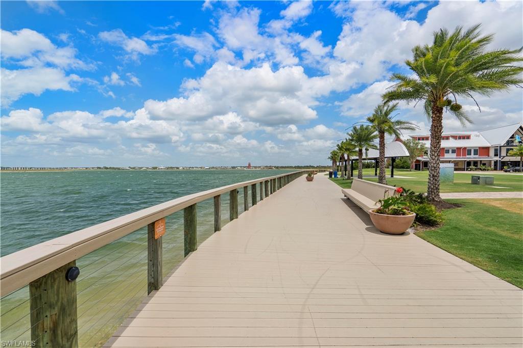 Waterfront boardwalk featuring a sturdy railing, mature palm trees, green lawn, and distant structures