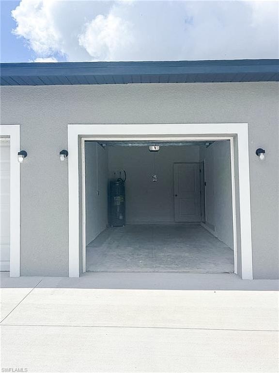 Spacious garage with a finished concrete floor, exterior stucco siding, and a white trim entry