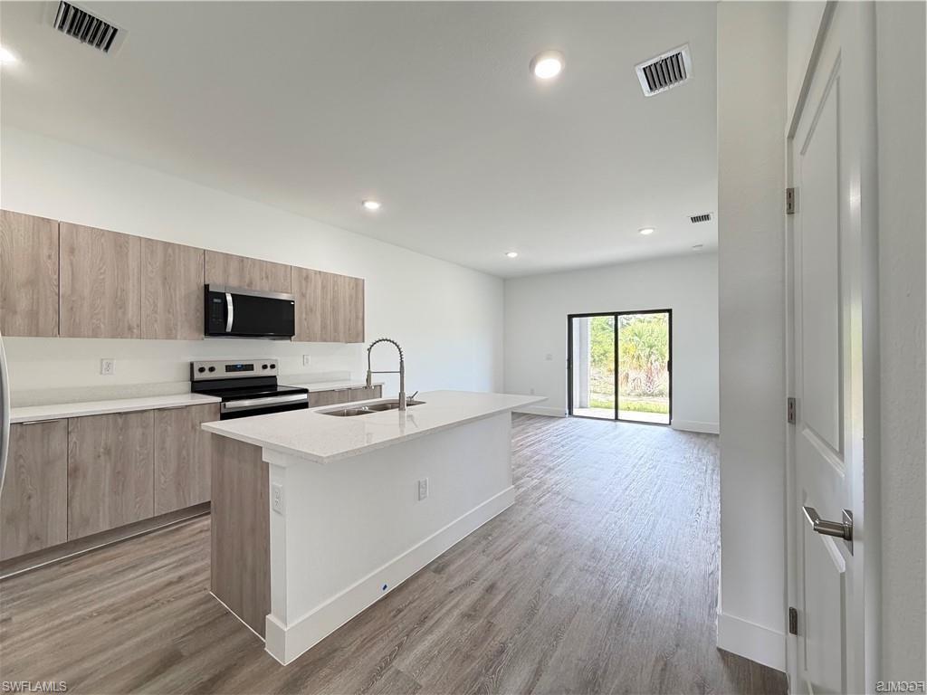 Modern kitchen featuring wood-finish cabinetry, stainless steel appliances, and a quartz countertop island with an integrated sink