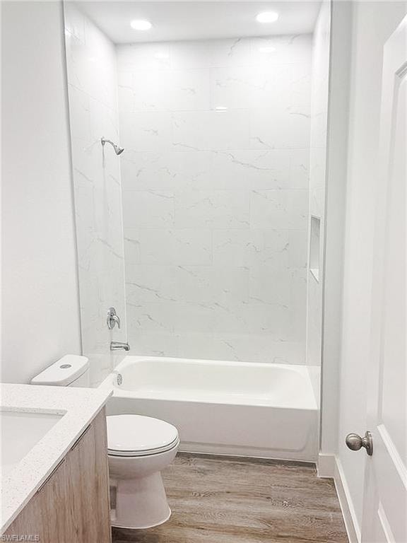 Bathroom featuring a white bathtub, marble-patterned tile shower surround, shower niche, wood-finish flooring, and recessed lighting