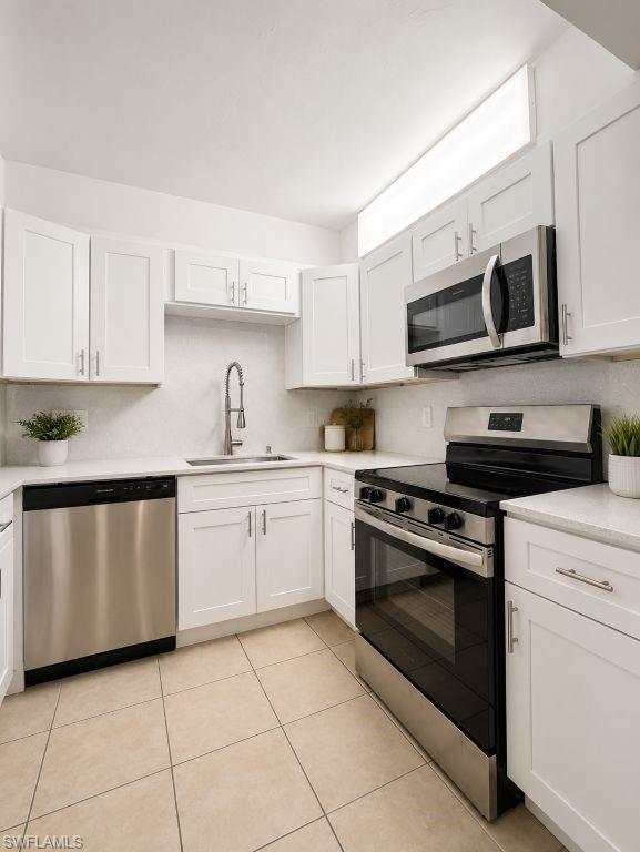 Modern kitchen featuring white shaker cabinetry, stainless steel appliances, a gooseneck faucet, light countertops, and square tile flooring