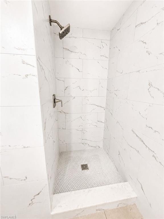 Walk-in shower featuring large format white tiled walls with subtle veining, a penny tile floor, and dark bronze fixtures