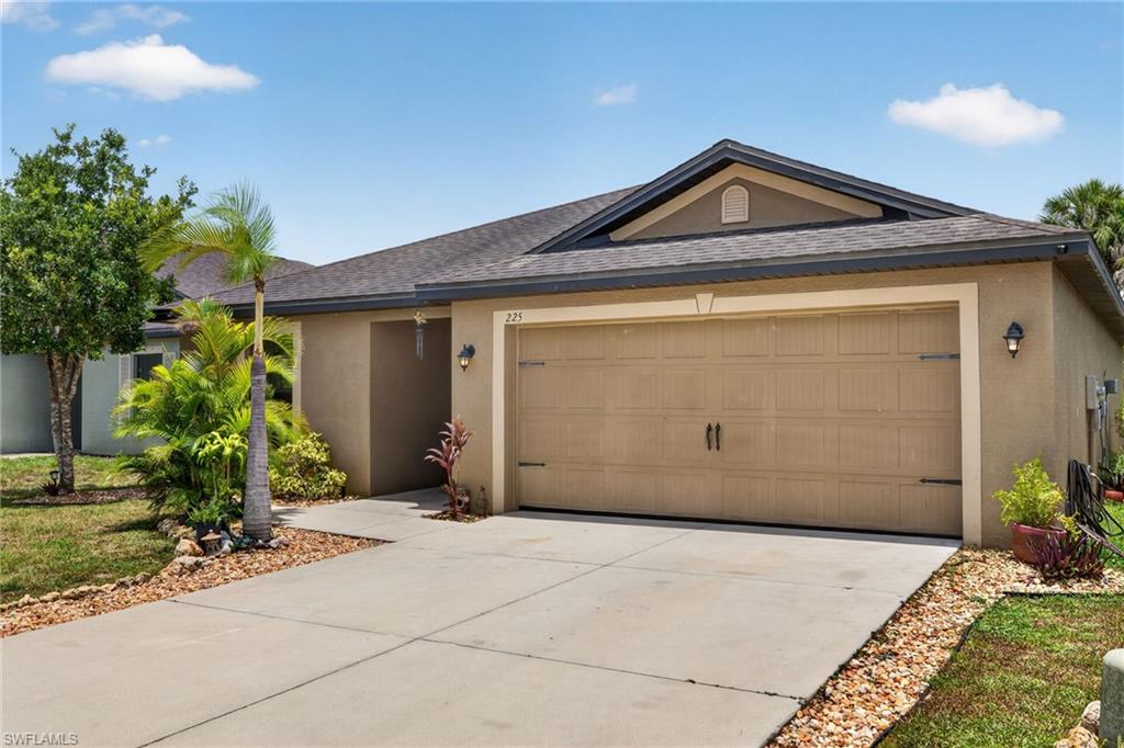 Stucco exterior featuring an attached two-car garage, concrete driveway, and established landscaping