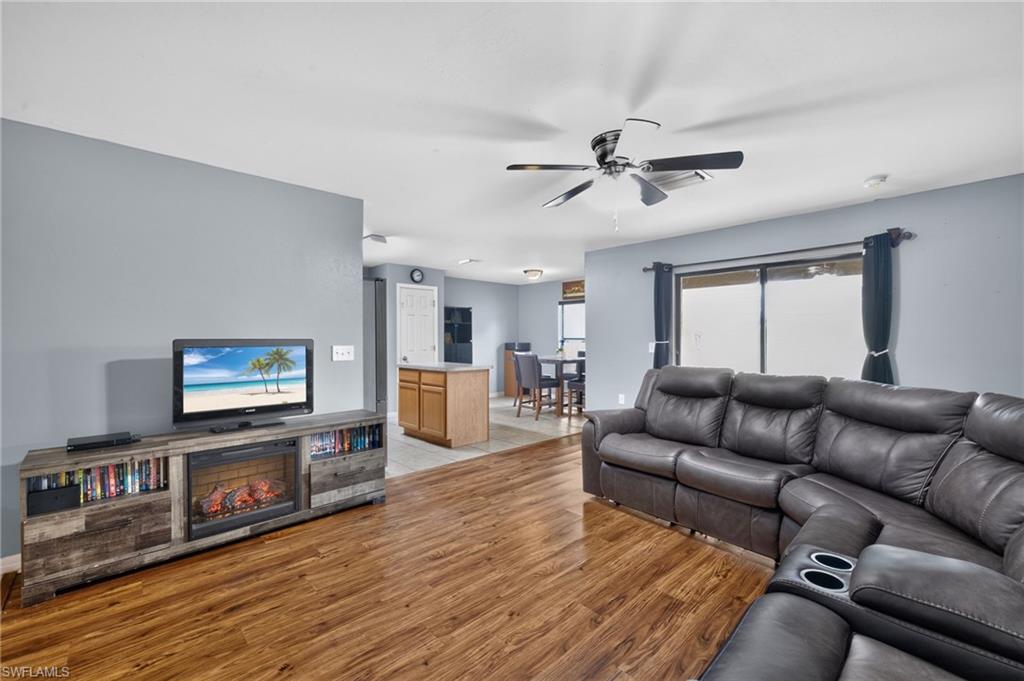 Open-concept living area featuring wood-finish flooring, a ceiling fan with integrated lighting, and a sliding glass door