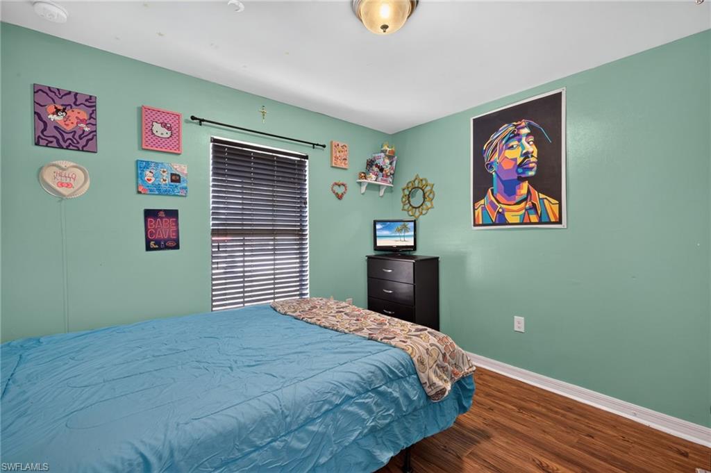 Bedroom featuring light green walls, wood-finish flooring, a window with horizontal blinds, and a flush mount ceiling light
