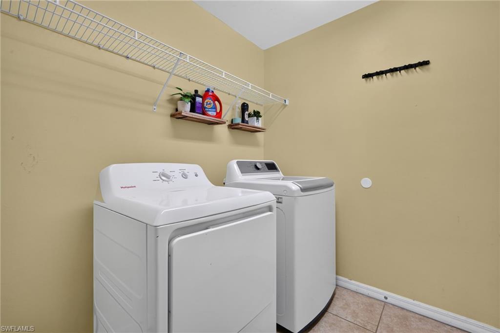 Dedicated utility space featuring a white top-load washer and dryer set, wire shelving, and tile flooring