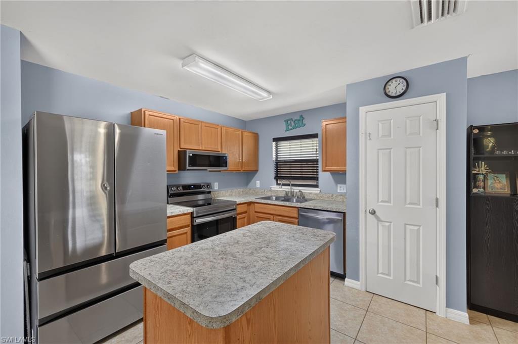 Kitchen featuring wood cabinetry, stainless steel appliances, a center island with a speckled countertop, and tiled flooring