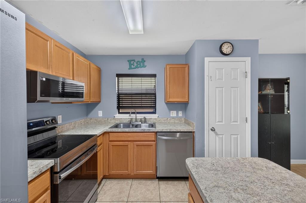 Kitchen featuring wood cabinetry, stainless steel appliances, speckled countertops, and tile flooring
