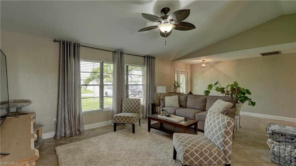 Vaulted ceilings featuring a ceiling fan with integrated lighting, tile flooring, and multiple windows with blinds