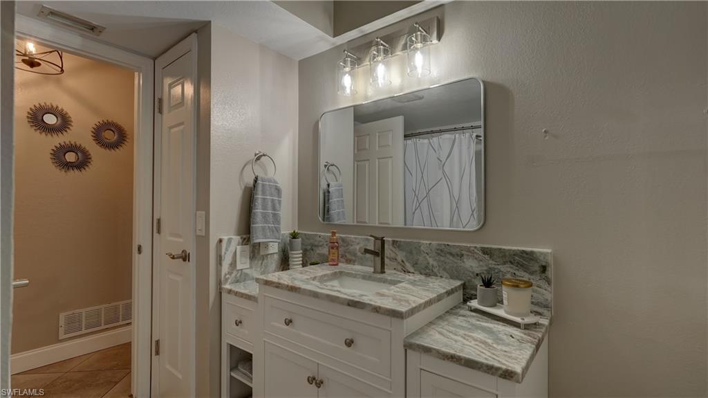Bathroom featuring a white vanity with an undermount sink, a bronze-finish faucet, and a stone countertop with a matching backsplash