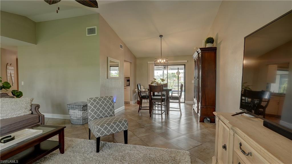 Vaulted ceiling living area featuring tile flooring, neutral wall paint, and a built-in ceiling fan