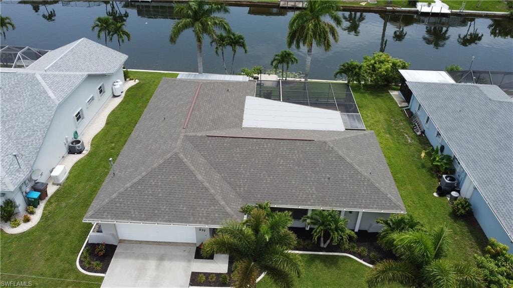 Waterfront property featuring a private boat dock, screened pool enclosure, mature palm trees, and an attached garage with concrete driveway