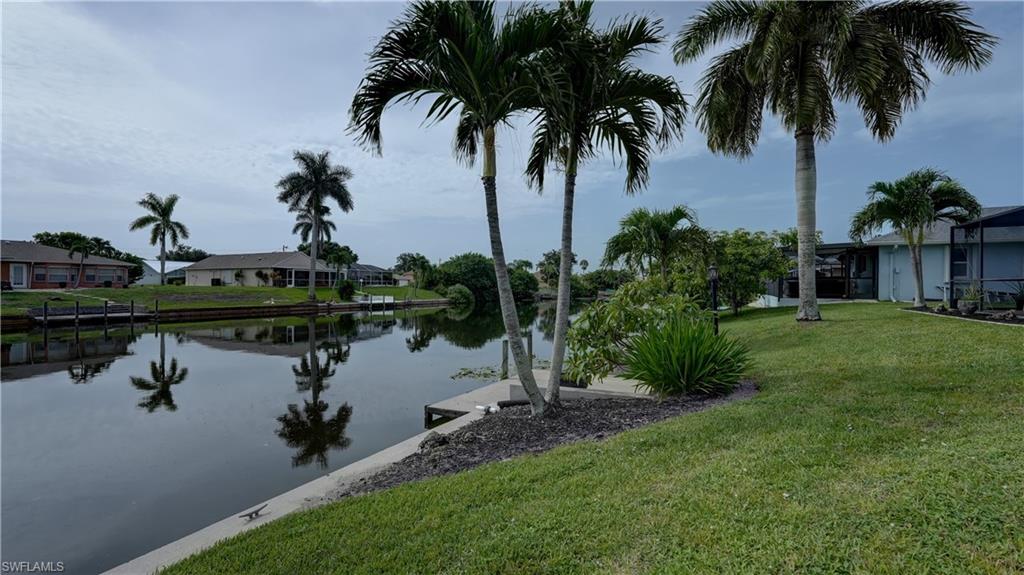 Waterfront property featuring a grassy lawn, palm trees, and a concrete seawall with a small dock