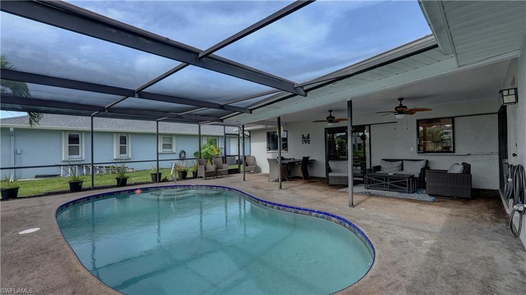 Screen-enclosed pool area featuring a freeform swimming pool with a tiled edge, a covered patio with two ceiling fans, and concrete pool decking