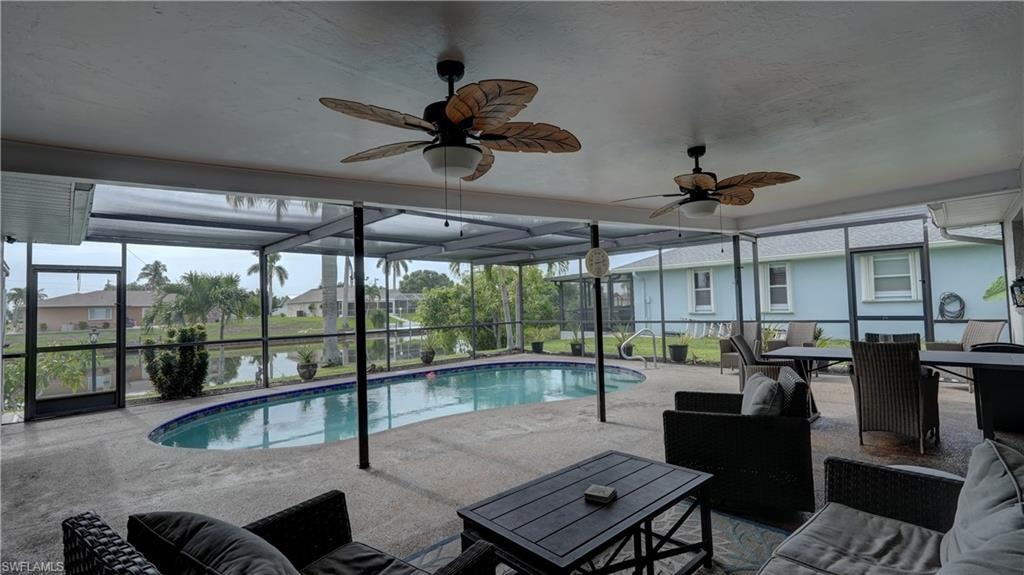 Screened-in outdoor living space featuring a freeform swimming pool, multiple ceiling fans, and a broad paved patio