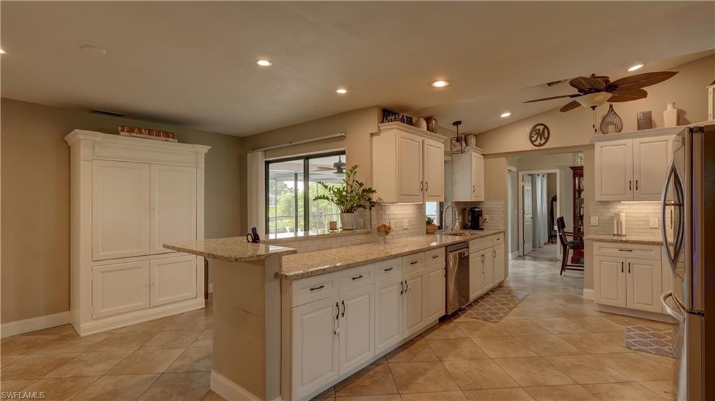 Spacious kitchen featuring white cabinetry, stone countertops, stainless steel appliances, tile flooring, and recessed lighting