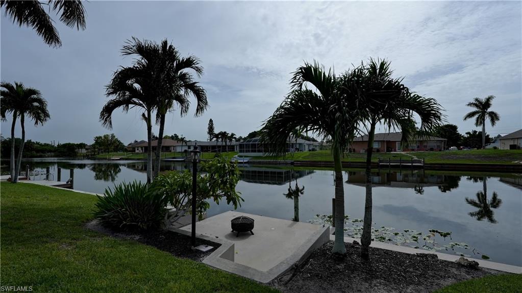 Waterfront property featuring a concrete patio, mature palm trees, manicured lawn, and a concrete dock